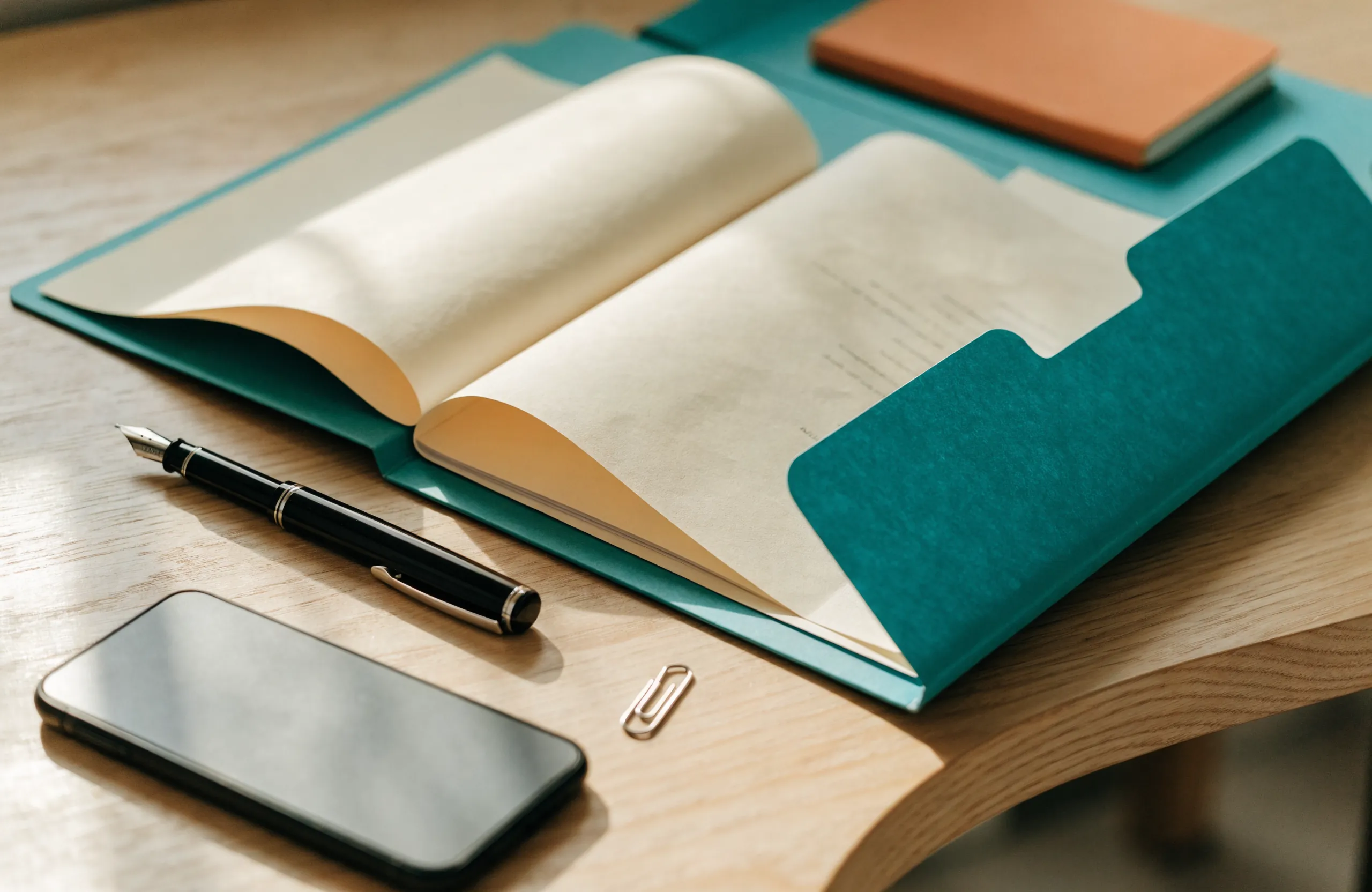 An organised folder of documents, a pen and a phone laid out on a desk